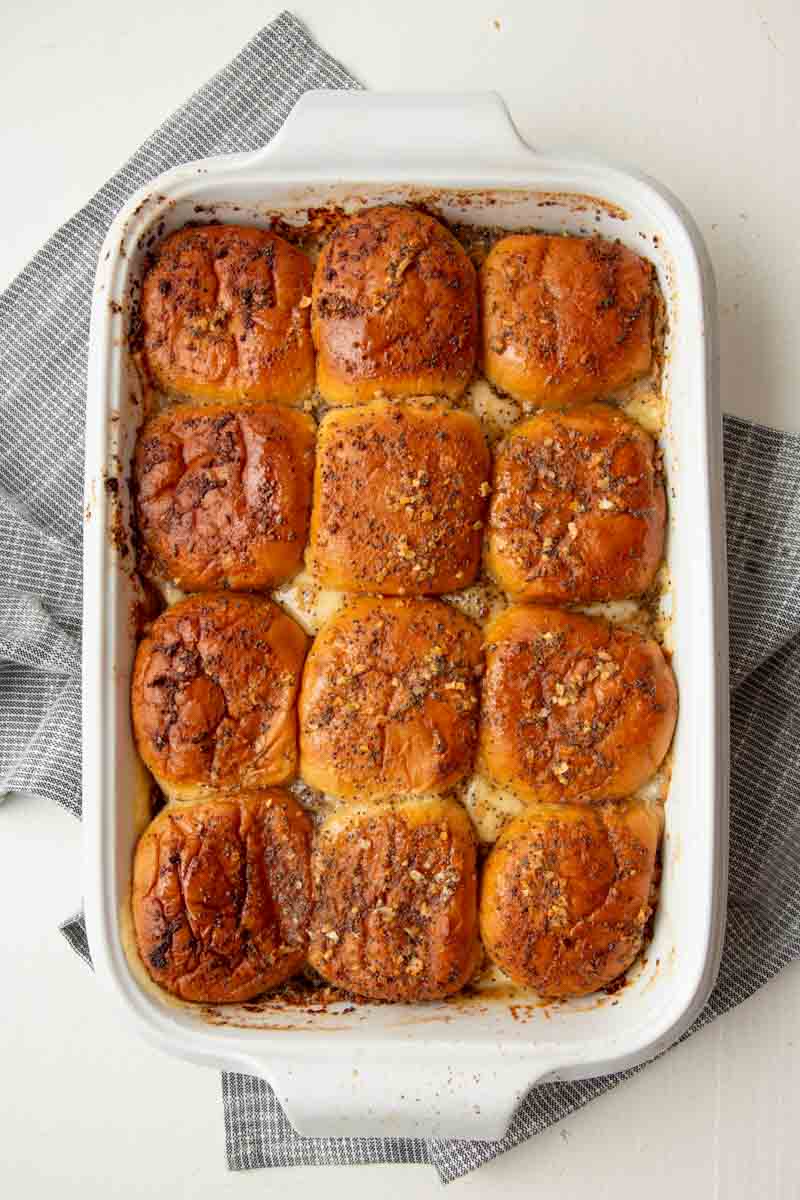 Top view of ham and swiss sliders nestled into a white baking dish on a black and white table linen.