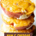 Close view of three ham and egg cups stacked on a light background. A text overlay reads, "Ham & Cheddar Egg Cups."