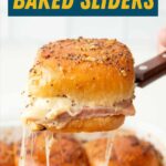 Close view of a spatula serving up a baked slider. A text overlay reads, "Ham & Cheese Baked Sliders."