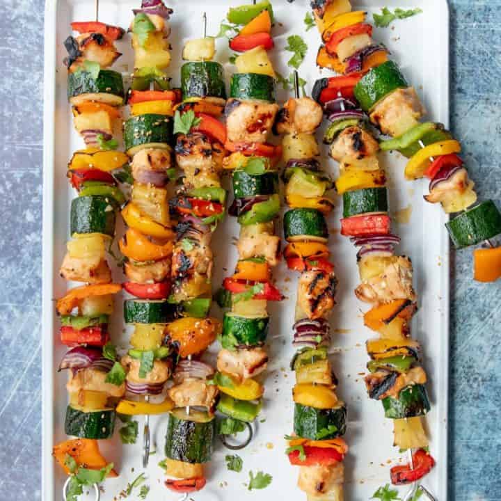 A white platter full of Grilled Hawaiian Chicken Kabobs on metal skewers