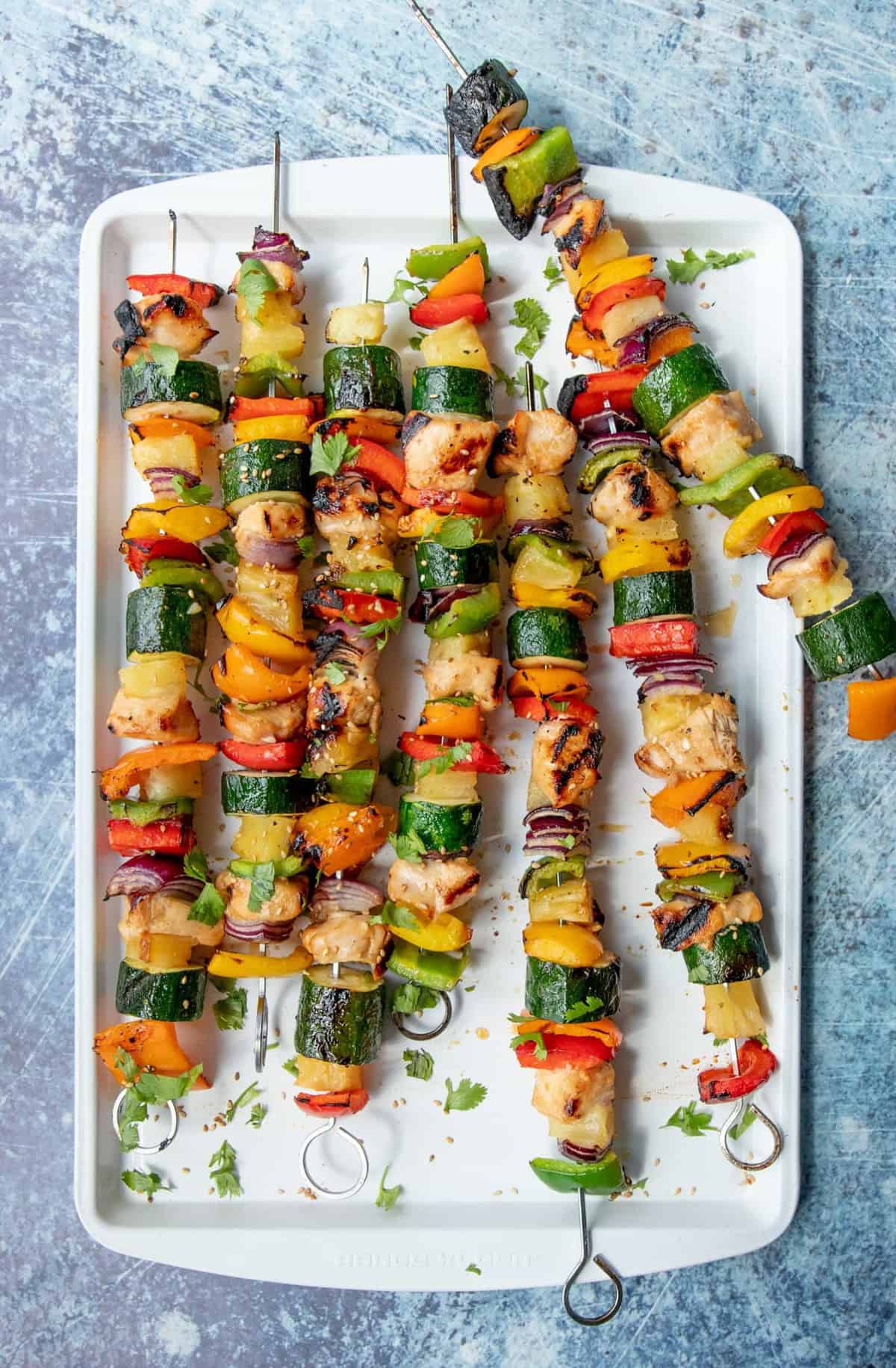 A white platter full of Grilled Hawaiian Chicken Kabobs on metal skewers