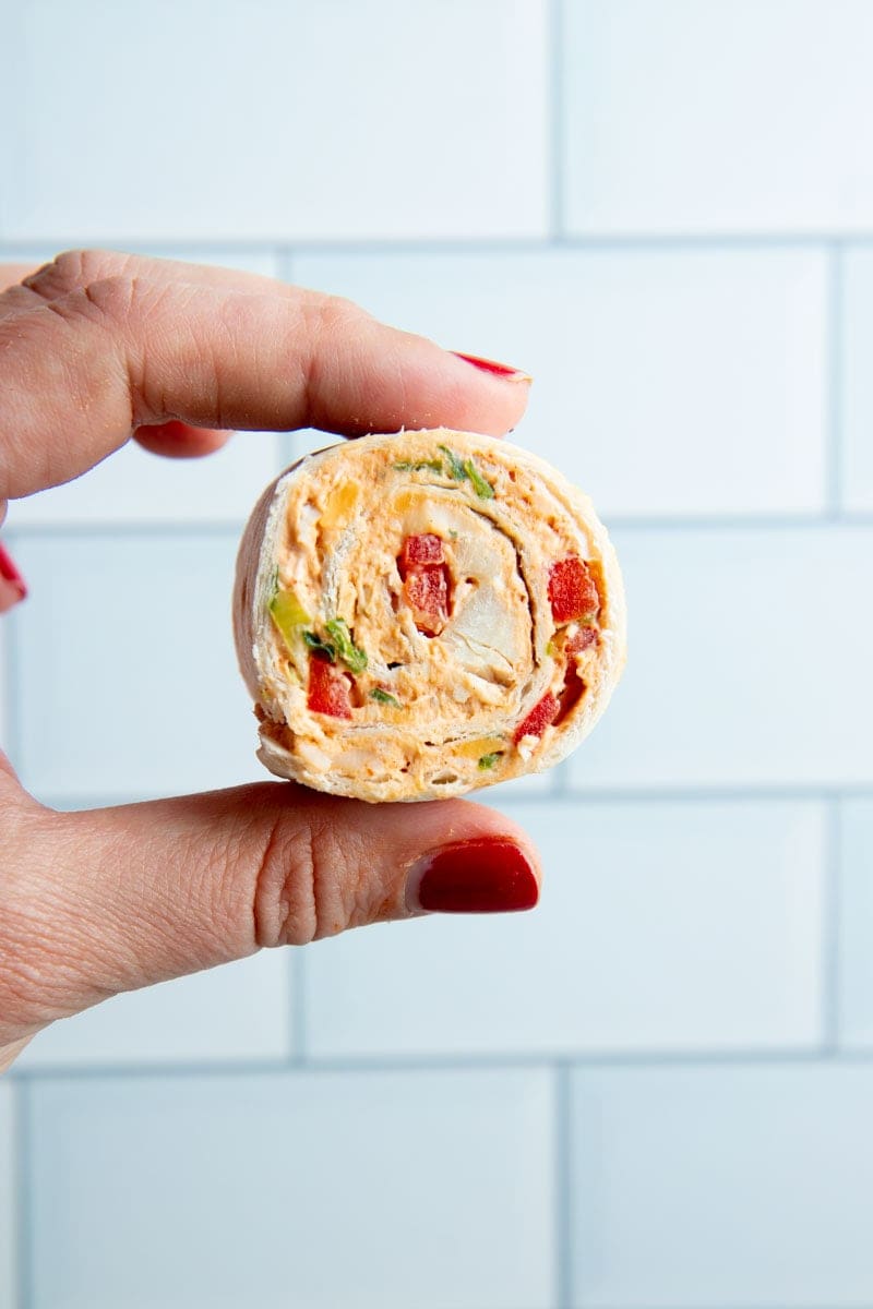 A hand holds up a taco pinwheel showing the colorful, creamy filling.