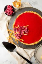 Overhead of cranberry tart on serving platter with candied garnishes on top of and beside it.