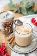 A glass mug filled with a chai latte sits in front of a jar of loose leaf chai mix.