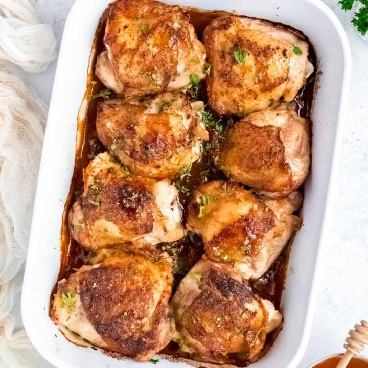 Honey garlic chicken thighs served in a white baking dish with additional honey on the side.