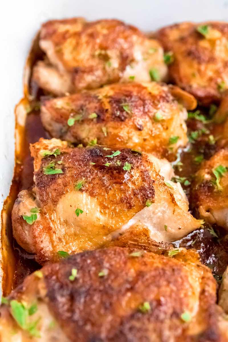 Tight view of skin on chicken thighs in a baking dish with a flavorful sauce.