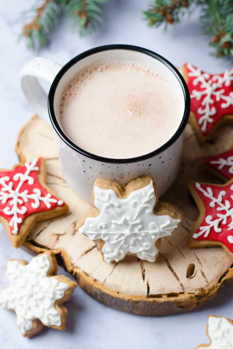 Enamelware mug of crockpot hot chocolate. Red and white decorated cookies surround the mug.