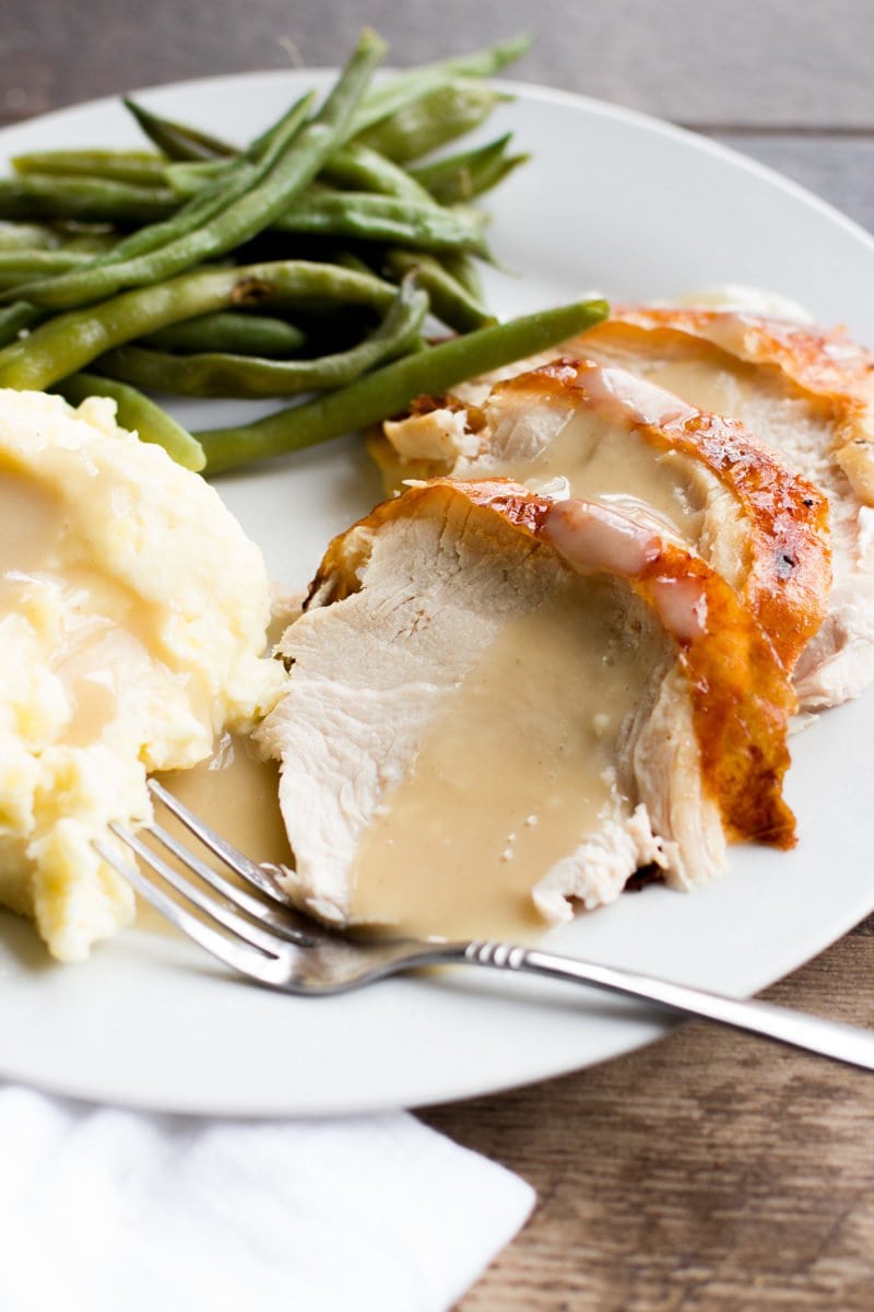 Slices of roasted turkey covered with gravy, on a plate with mashed potatoes and green beans