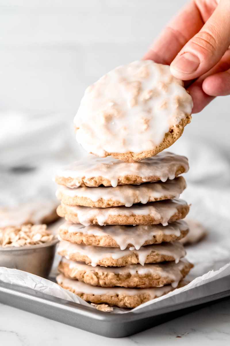 A hand takes an iced oatmeal cookie from a stack of cookies on a tray.