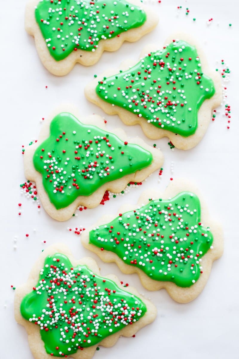 Sugar cookies in the shape of Christmas trees are decorated with green icing and sprinkles.