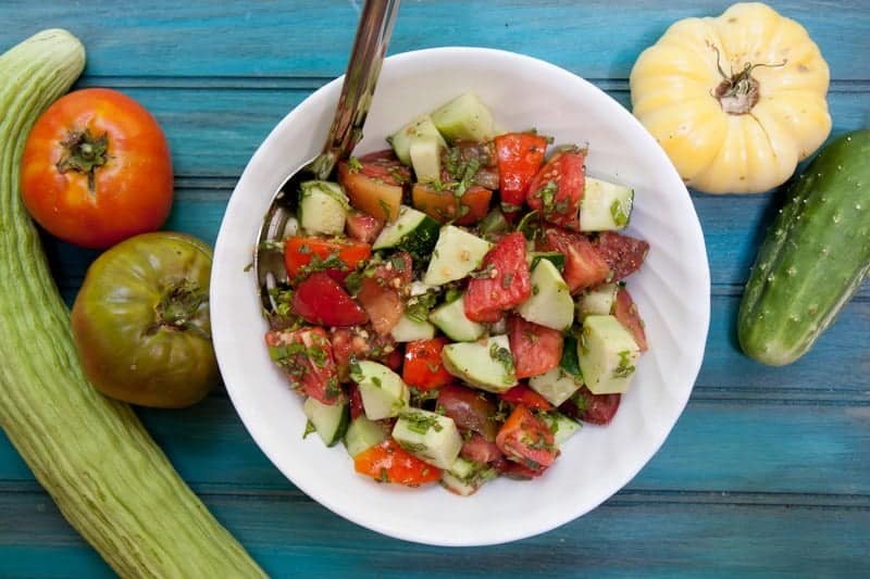 Cucumber tomato salad in a white bowl on a teal backdrop