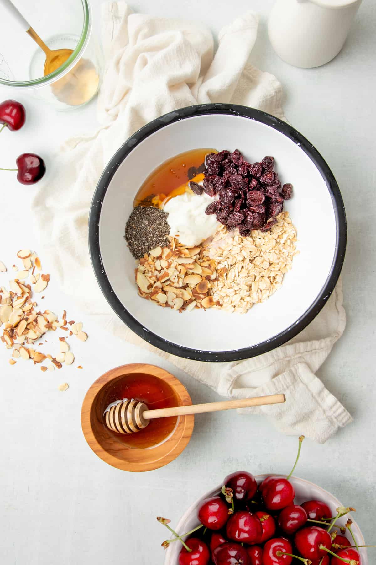 White mixing bowl full of ingredients such as oats, Greek yogurt, chia seeds, dried cherries, and more. 