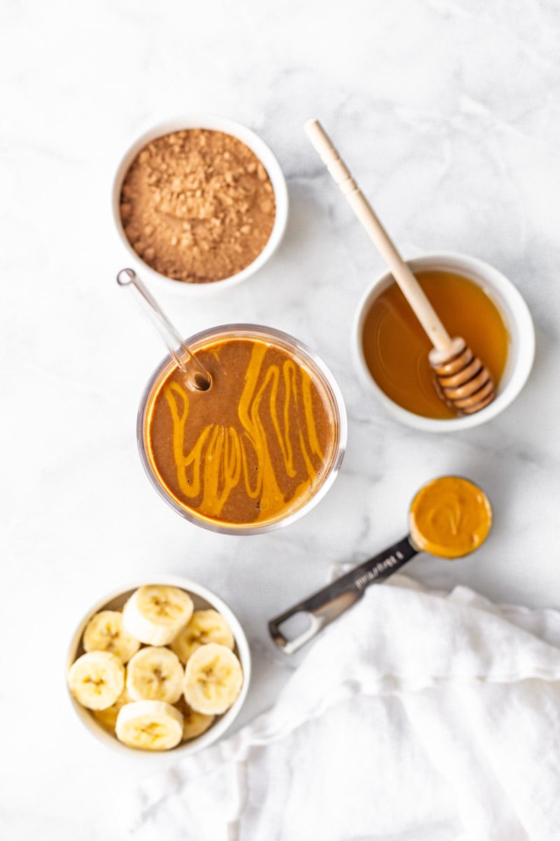 Overhead of finished chocolate peanut butter smoothie with smoothie ingredients around it.