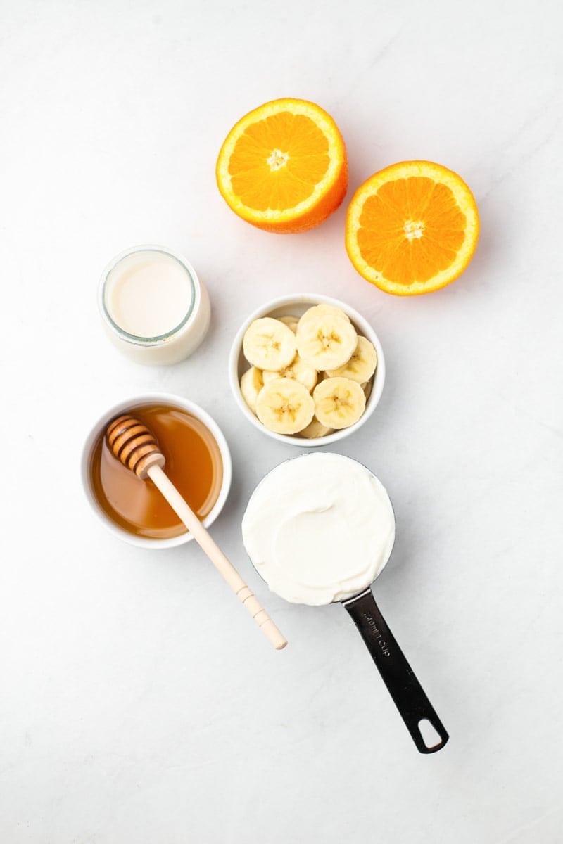 Overhead of the five ingredients needed to make an orange smoothie.