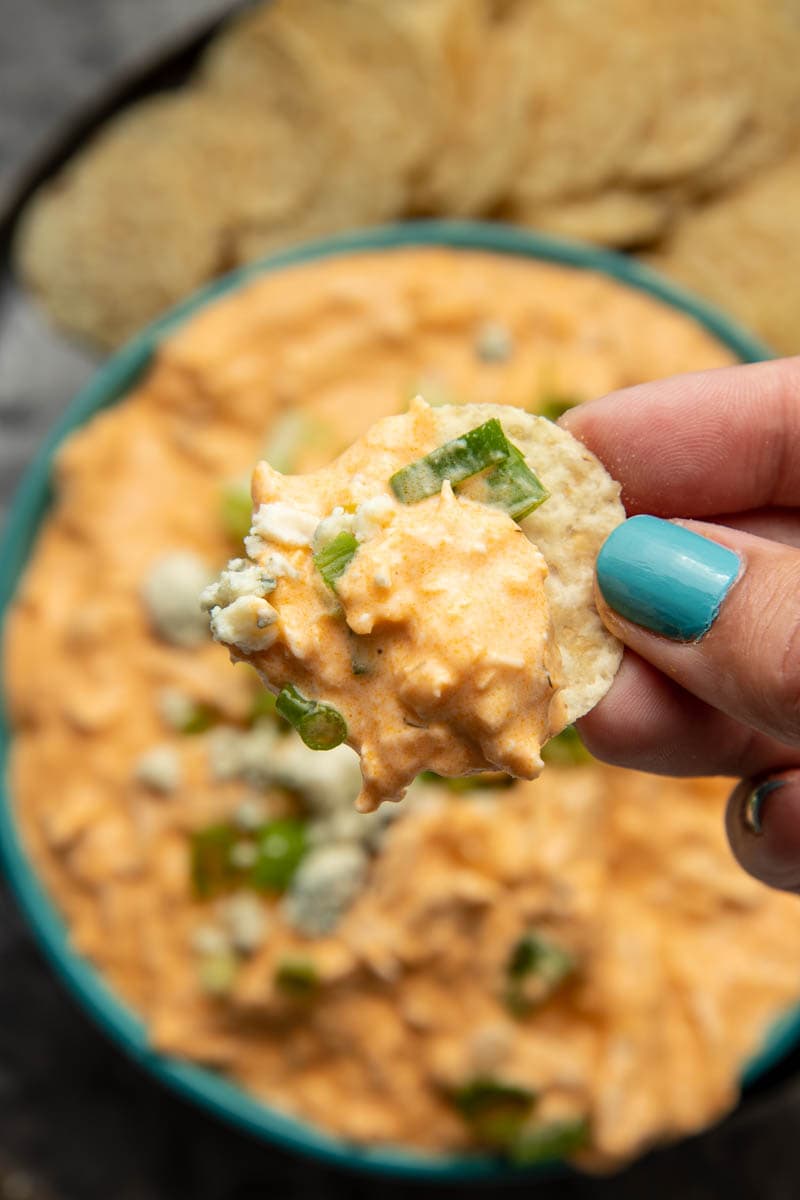 Close view of a hand holding a tortilla chip loaded with a bite of homemade buffalo chicken dip.