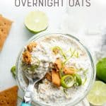 A spoon with a blue handle sits in a jar of key lime pie overnight oats. A text overlay reads, "Key Lime Pie Overnight Oats."