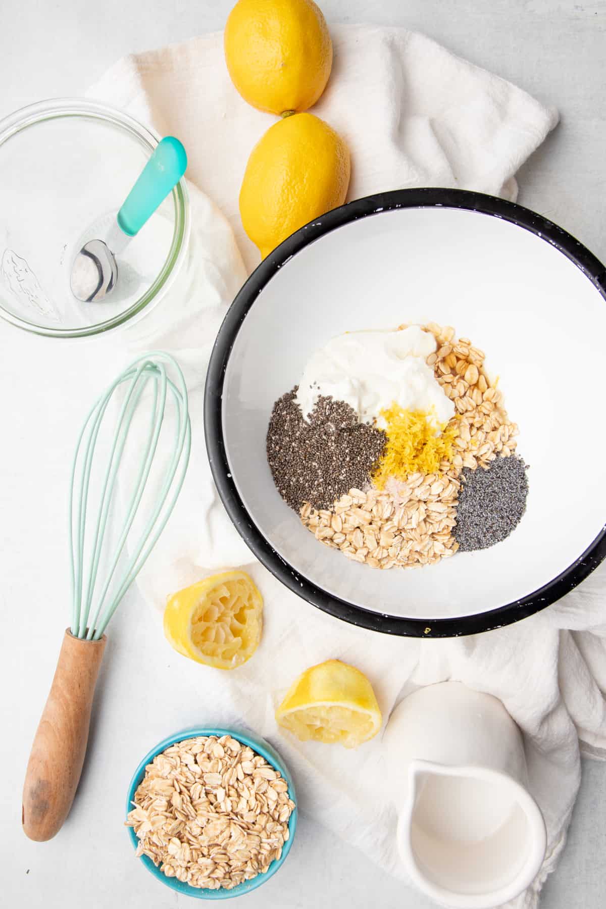 Ingredients for lemon poppyseed overnight oats sit in a white bowl. A whisk sits beside the bowl.