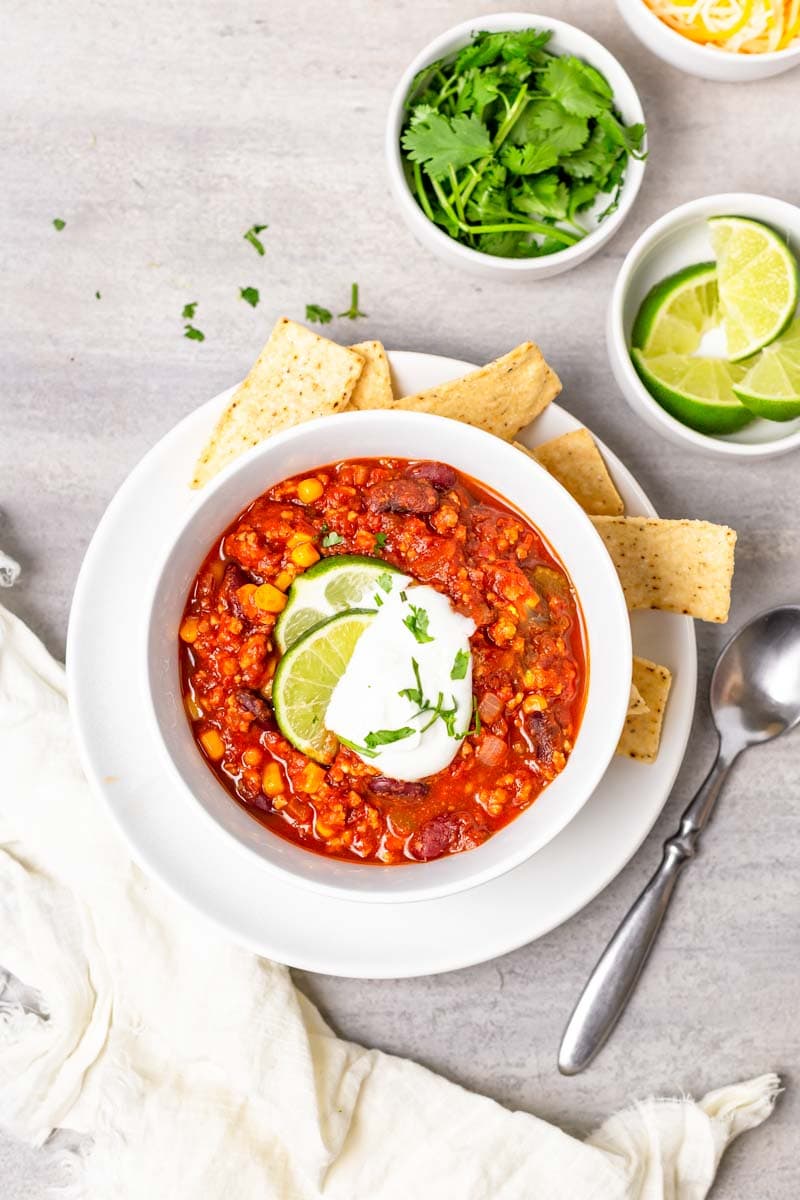 Overhead of a full bowl of finished turkey chili with spoon and linen napkin alongside.