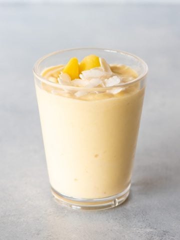 Top view of a mango smoothie topped with coconut flakes and mango pieces in a tall glass.