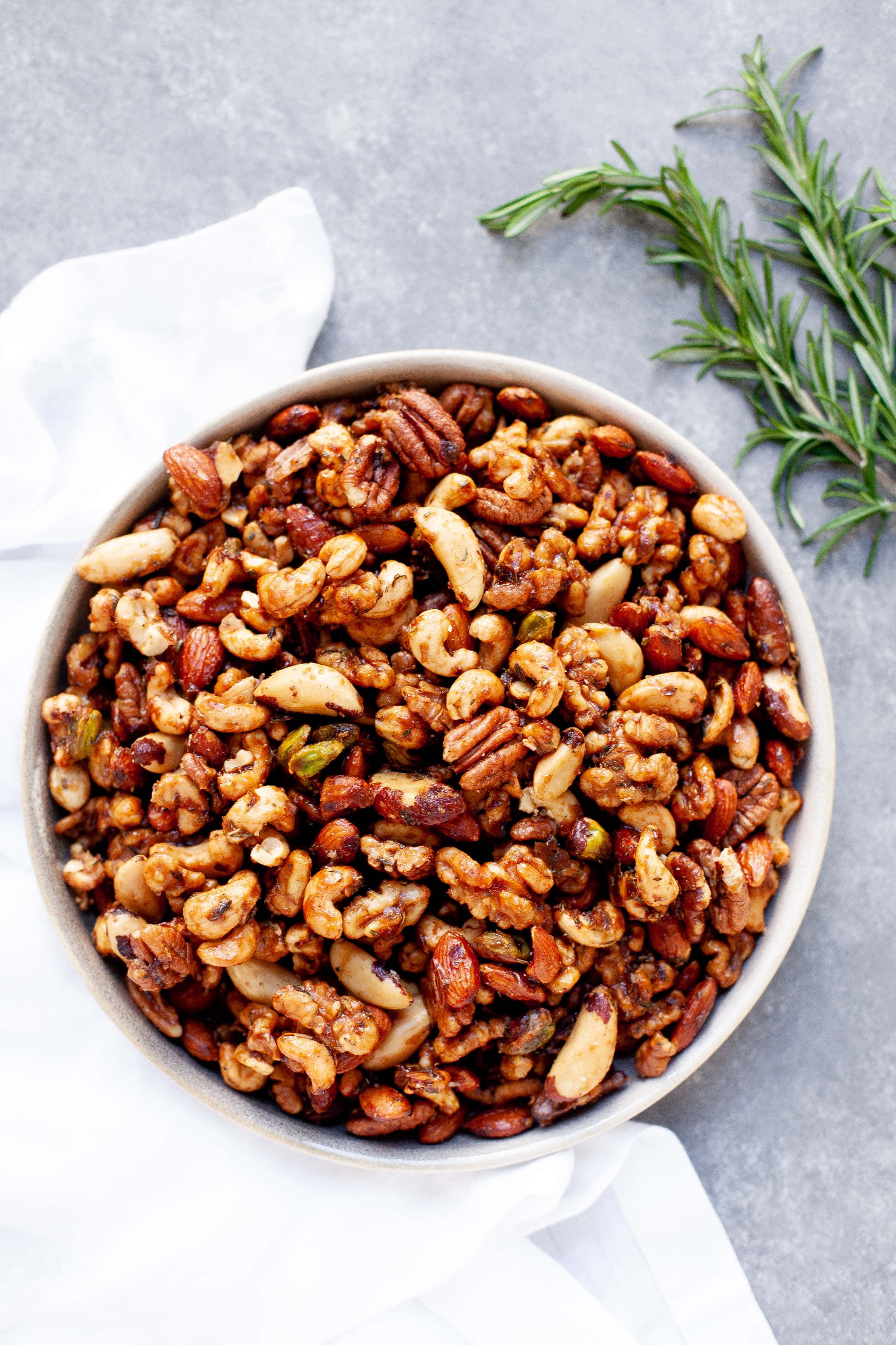 White bowl full of Maple Rosemary Bar Nuts, with sprigs of rosemary nearby