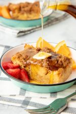 Pouring maple syrup over a single slice of french toast casserole with fresh fruit.