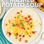 Close view of a bowl of soup with loaded toppings such as cheese, crumbled bacon, and scallions with a bread basket nearby. A text overlay reads, "Leftover Mashed Potato Soup."