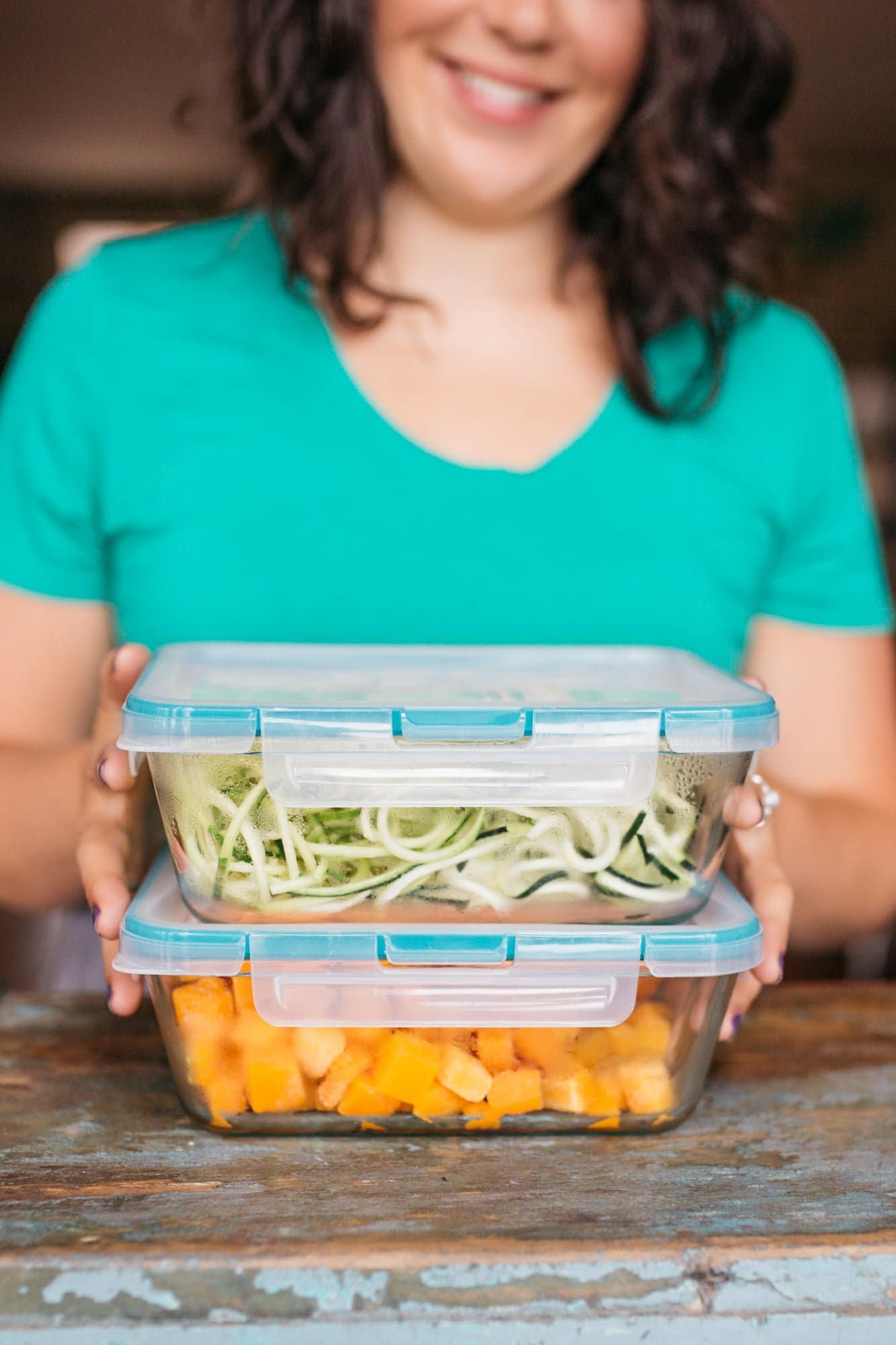 Close-up of a woman holding glass containers. One is filled with zucchini noodles, and the other with sweet potato cubes.