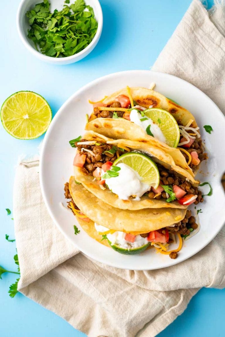 Overhead of a plate full of three vegetarian tacos on a kitchen linen with fresh lime and cilantro.