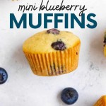 Close view of a mini blueberry muffin on its side with fresh berries and additional muffins around it. A text overlay reads, "Mini Blueberry Muffins."