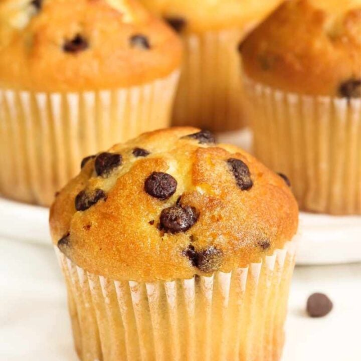 Close view of a mini chocolate chip muffin on a white counter with additional chocolate chips around it.