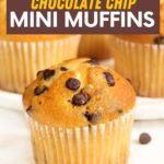 Close view of a mini chocolate chip muffin on a white counter with additional chocolate chips around it. A text overlay reads, "Chocolate Chip Mini Muffins."