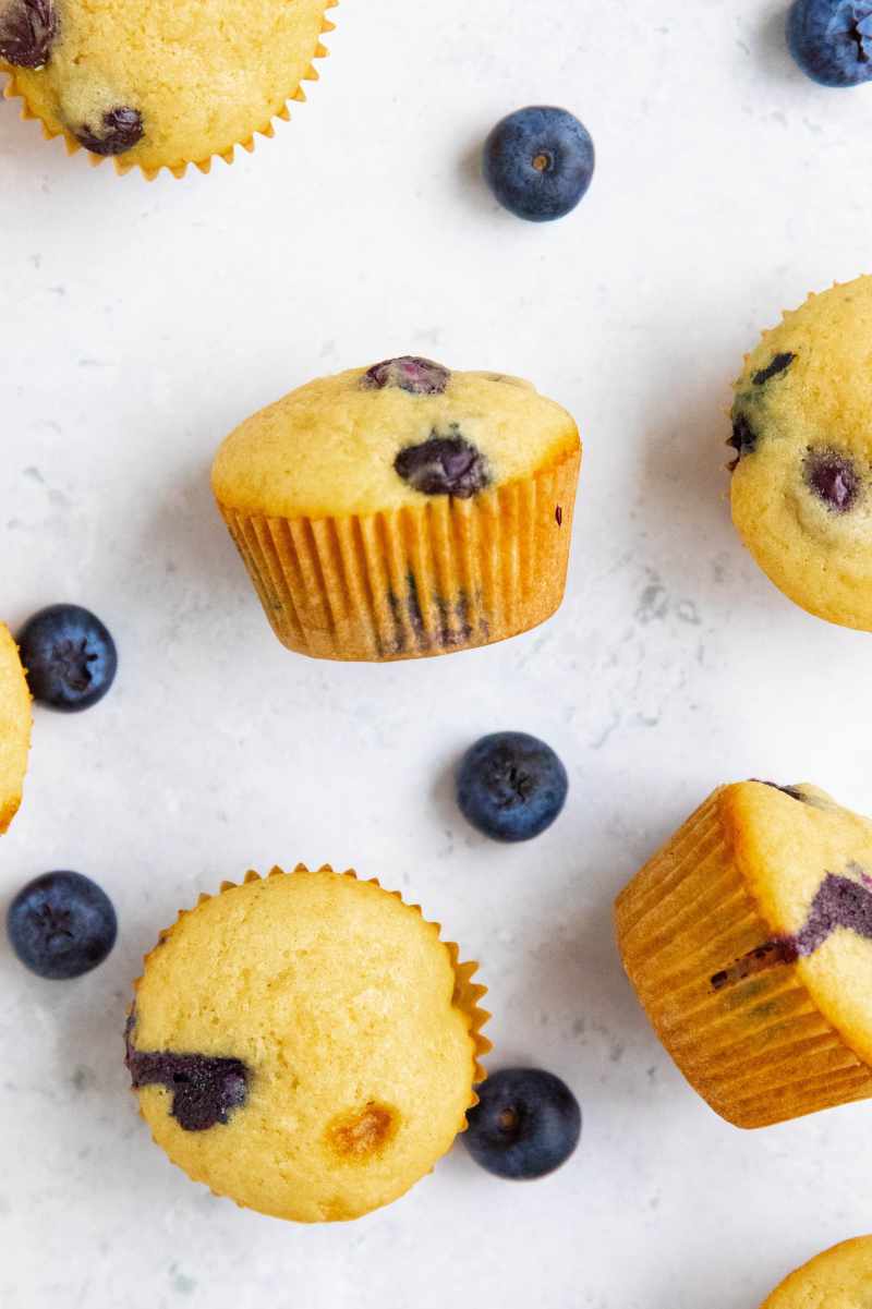 Mini muffins, some standing and some on their sides, on a counter with fresh berries around them.