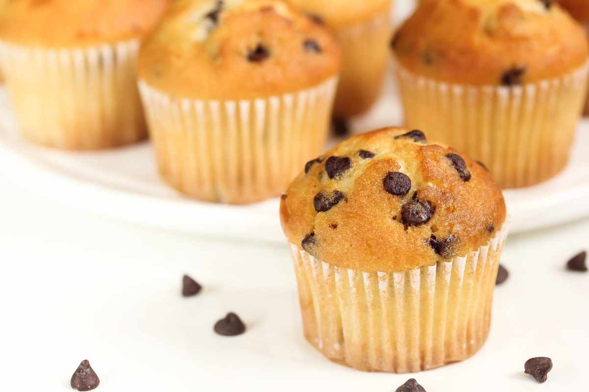 Tight view of a mini muffin on a white counter with chocolate morsels around it.