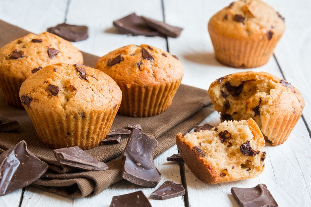 Three muffins on a linen napkin with one split muffin alongside with pieces of chocolate nearby.