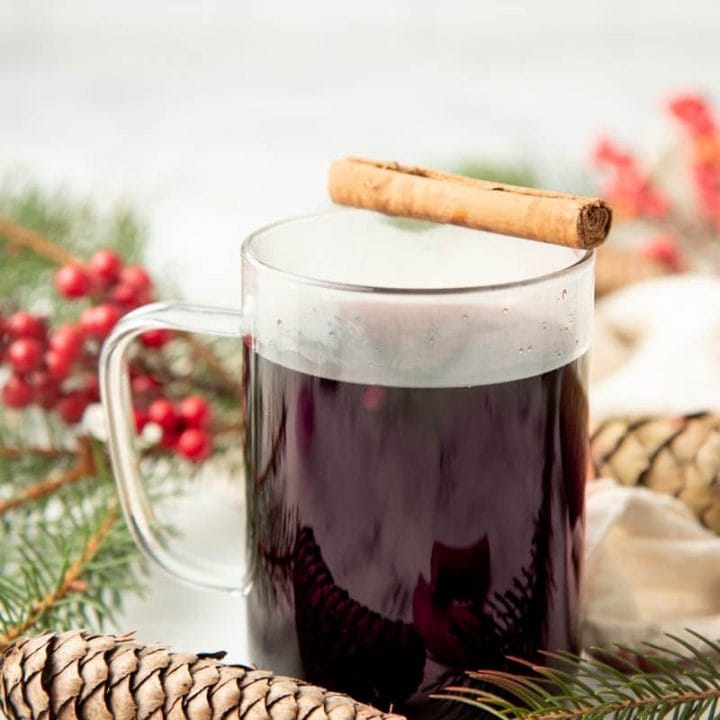 A mug of Christmas wassail sits with a cinnamon stick balanced across the rim.