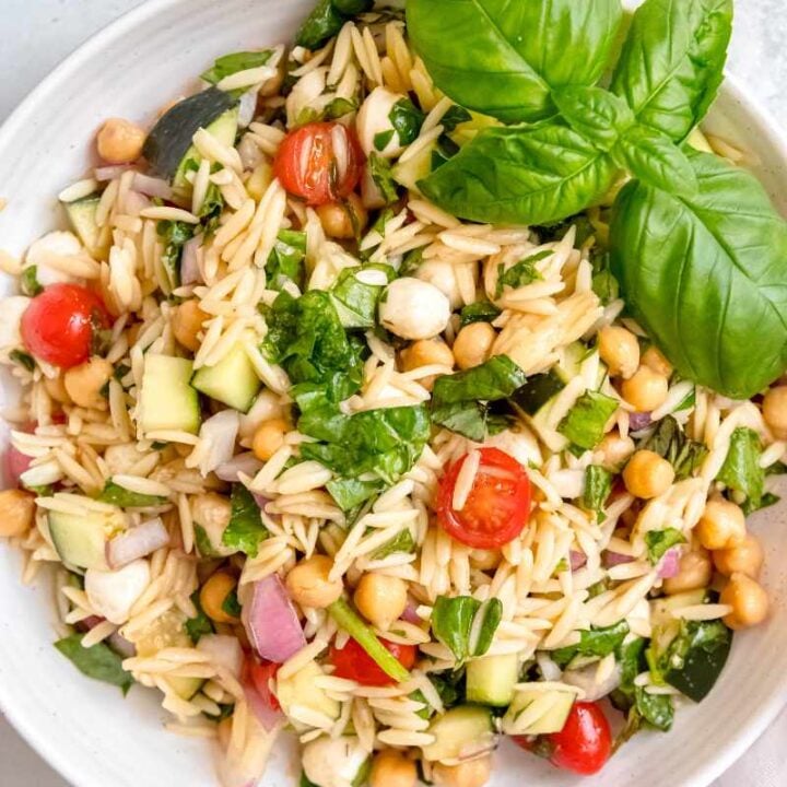 Overhead of orzo pasta salad in a white bowl on a light countertop.