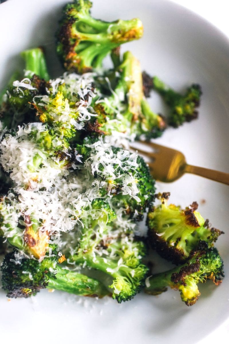 Roasted broccoli topped with parmesan cheese on a white serving dish with a gold fork alongside.