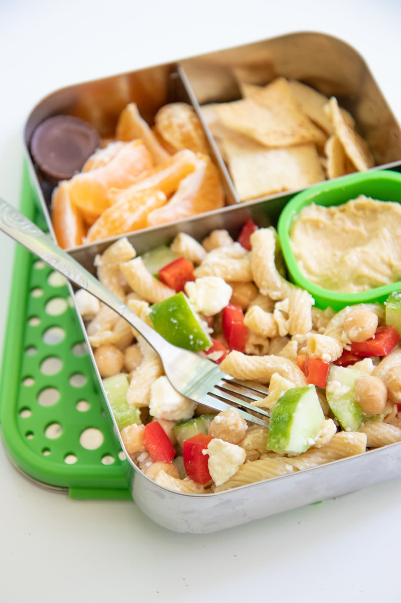 Stainless steel lunchbox with pasta salad, orange slices, and pita chips.