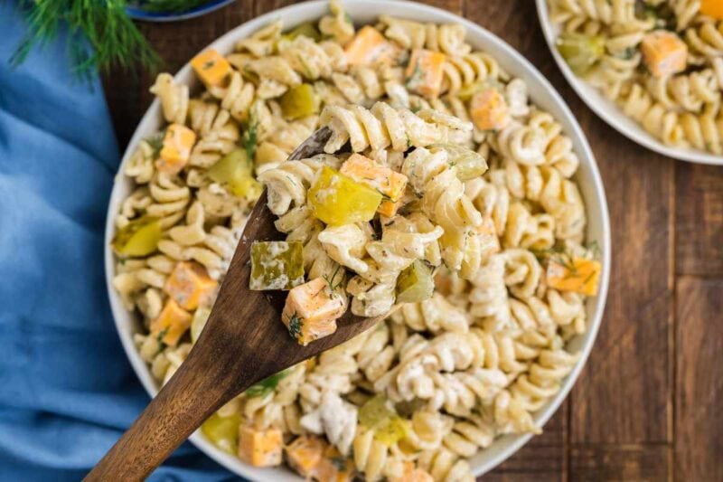 Close view of a wooden spoon holding a scoop of pasta salad above a bowl of more salad.