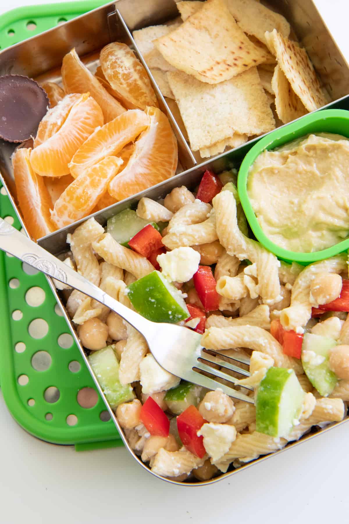 Stainless steel lunchbox with pasta salad, orange slices, and pita chips for a school lunch.