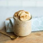 A small, gold, dessert spoon rests next to a jar of peanut butter banana overnight oats.