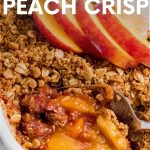 A serving spoon dips into the corner of a pan holding fresh peach crisp. A text overlay reads "Fresh Peach Crisp"