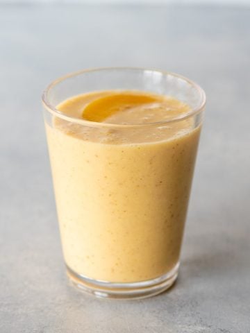 Top view of a peach smoothie in a glass with a peach slice on top.