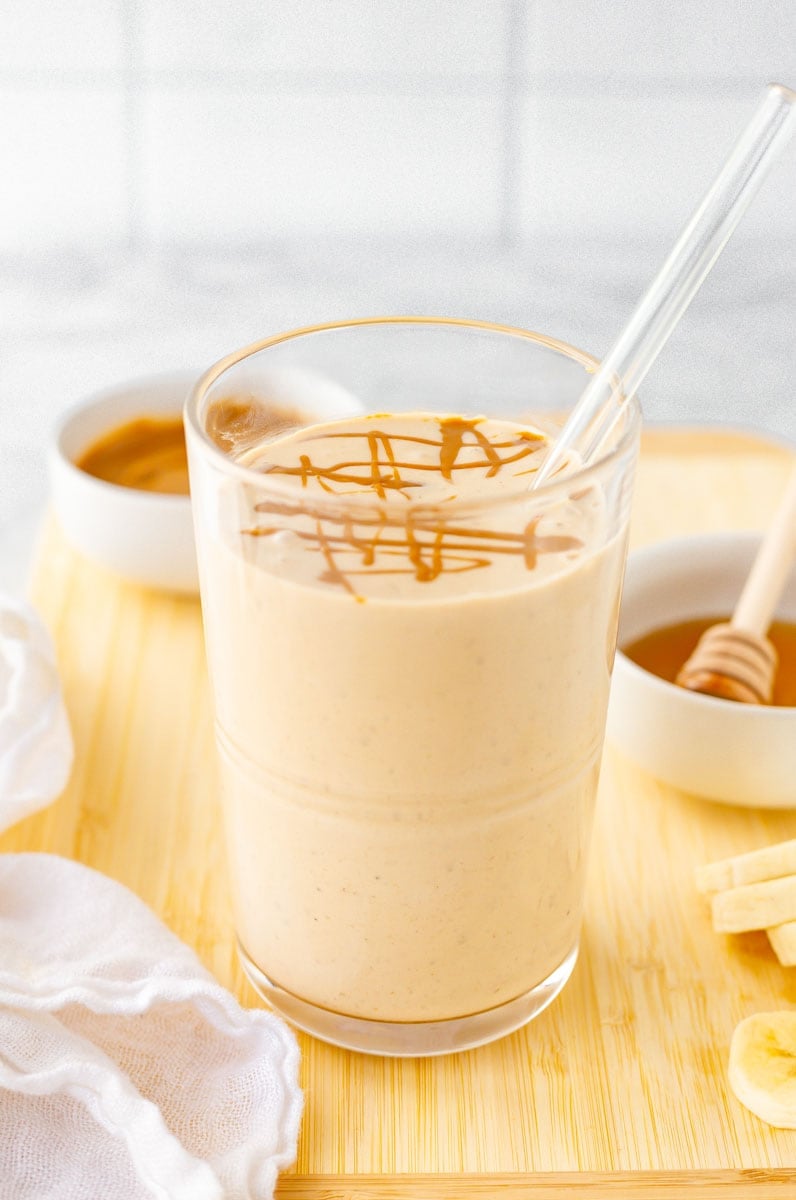 Close-up of smoothie with glass straw on cutting board with fresh ingredients.