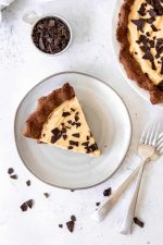 Overhead of a slice of peanut butter pie garnished with chocolate pieces on a ceramic plate with two forks nearby.