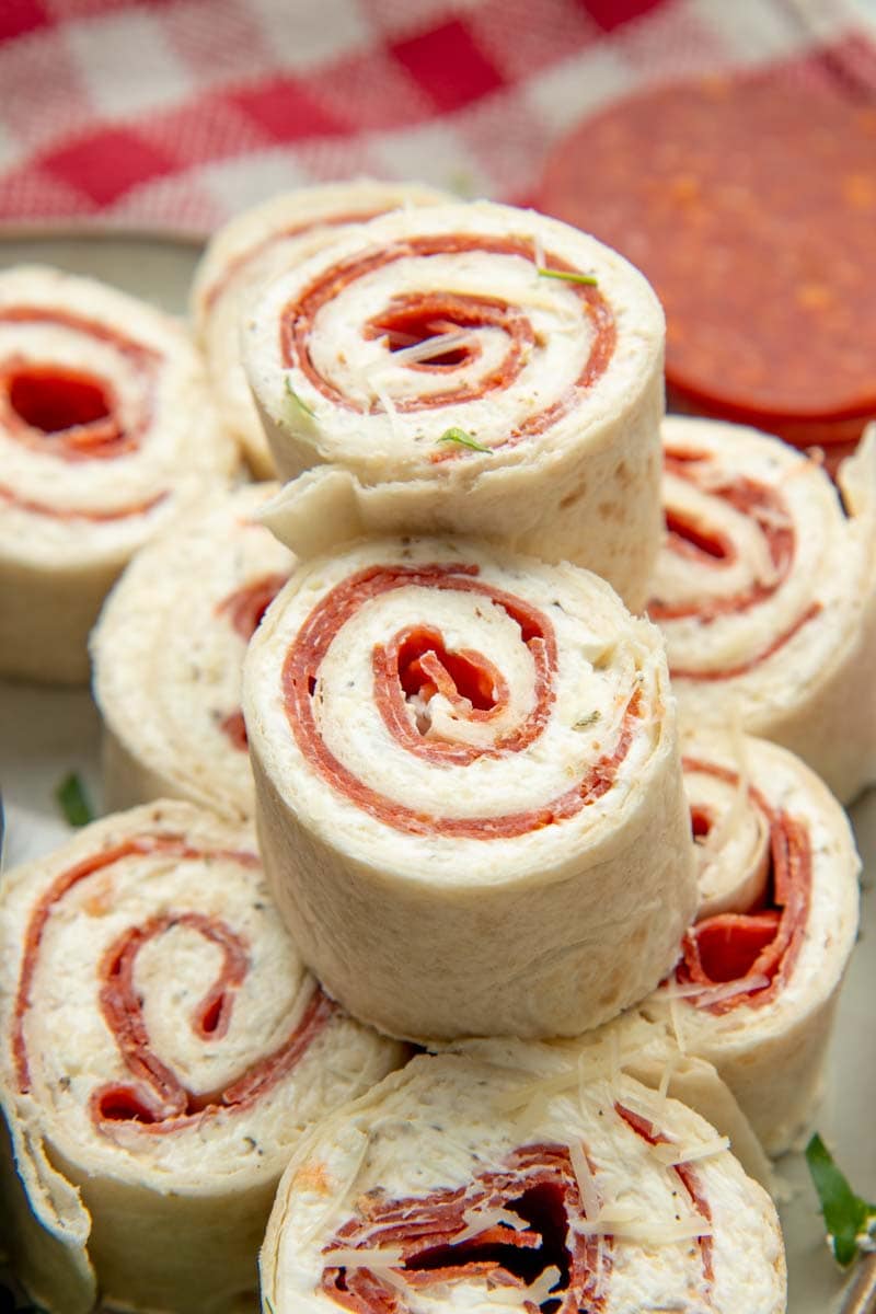 Pepperoni pinwheels stacked on a plate with two pinwheel bites on top.