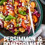 A fork rests on a dark bowl, filled with persimmon and pomegranate salad. A text overlay reads "Persimmon & Pomegranate Spinach Salad."