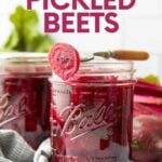 A fork rests across the top of an open canning jar, a pickled beet slice speared on the end of it. A text overlay reads, "Homemade Pickled Beets."