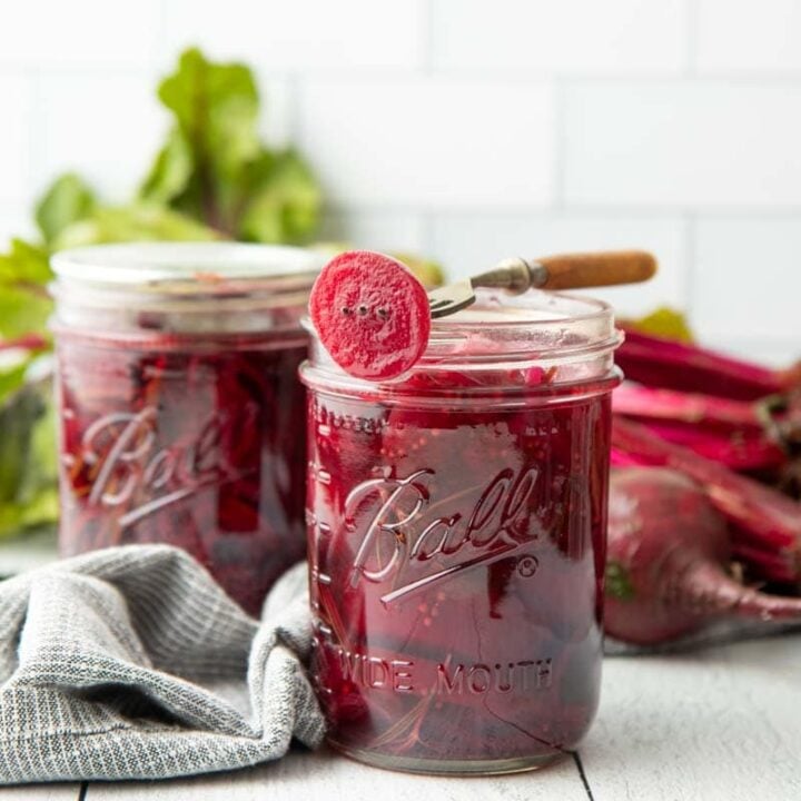 A fork rests across the top of an open canning jar, a pickled beet slice speared on the end of it.