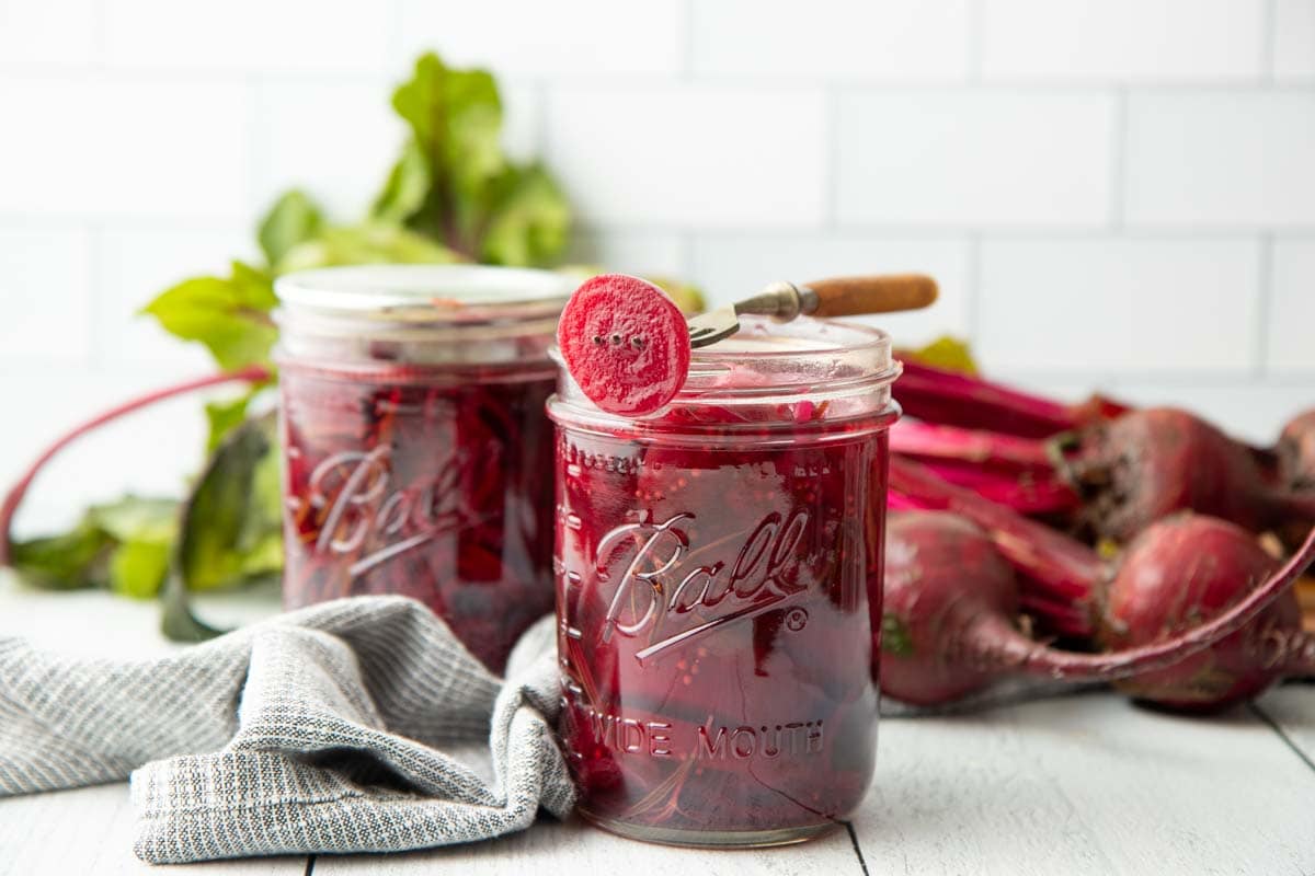 A fork rests across the top of an open canning jar, a pickled beet slice speared on the end of it.